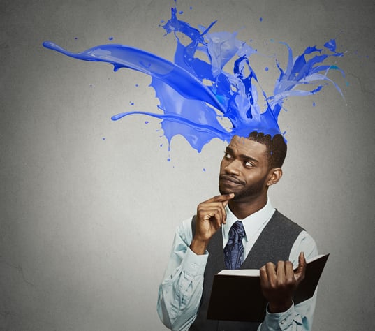 Thoughtful businessman reading book has crazy creative idea looking up colorful splashes coming out of his head isolated on gray wall background